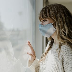 woman with medical mask looking out window